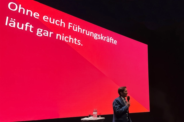 Eine Rede bei der Präsentation der Rewe Design Umsetzungen, im Hintergrund ist auf der Präsentation zu lesen: "Ohne euch Führungskräfte läuft gar nichts."